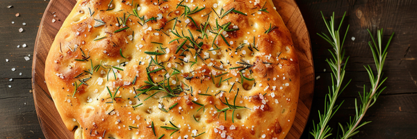 Focaccia mit Rosmarin und Rosé Salzflocken auf Holzplatte – frisch gebacken und goldbraun